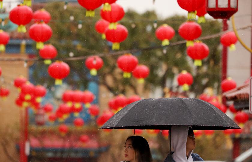 LOS ANGELES, CALIF. - MAR. 14, 2023. Pedestrians wait to cross Hill Street in Chinatown as an atmospheric river brings heavy rain to Southern California on Tuesday, Mar. 14, 2023. (Luis Sinco / Los Angeles Times)