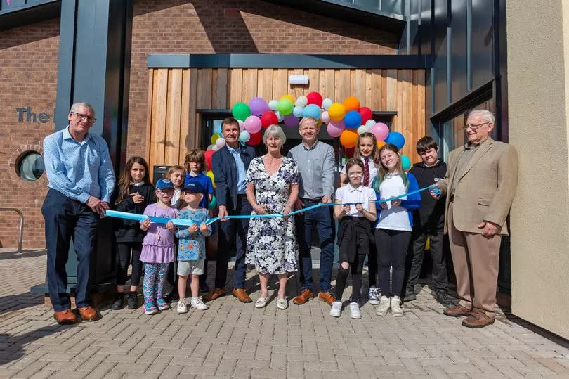 Large group photo outside building. People smiling in front of large colourful balloon arch. Morag Murdoch is pictured in the centre with large scissors cutting a ribbon