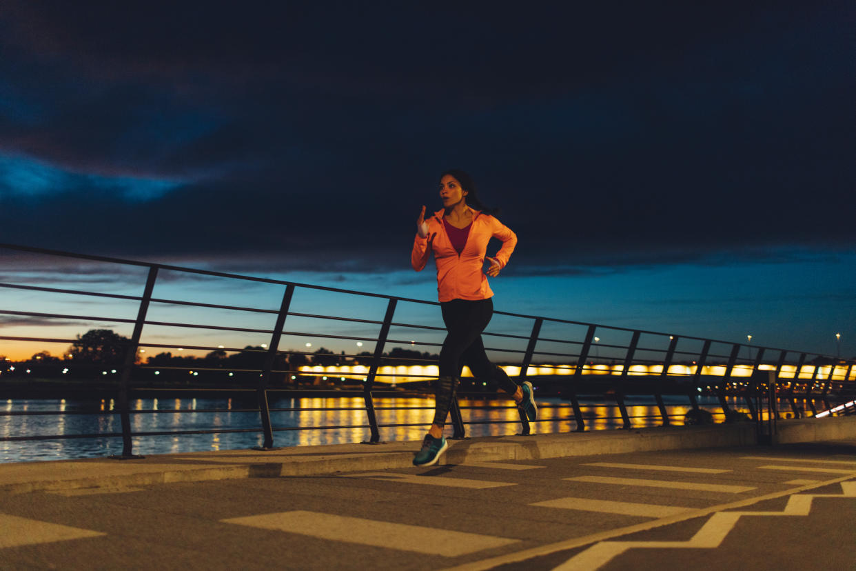 A runner striding after dark along a waterway. 