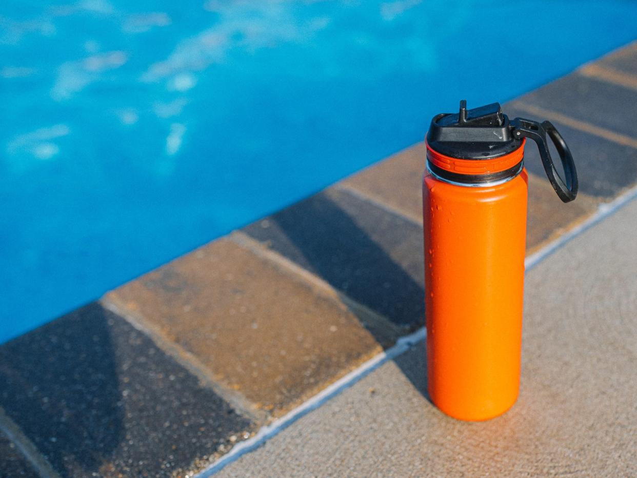 Orange water bottle by the side of a pool.