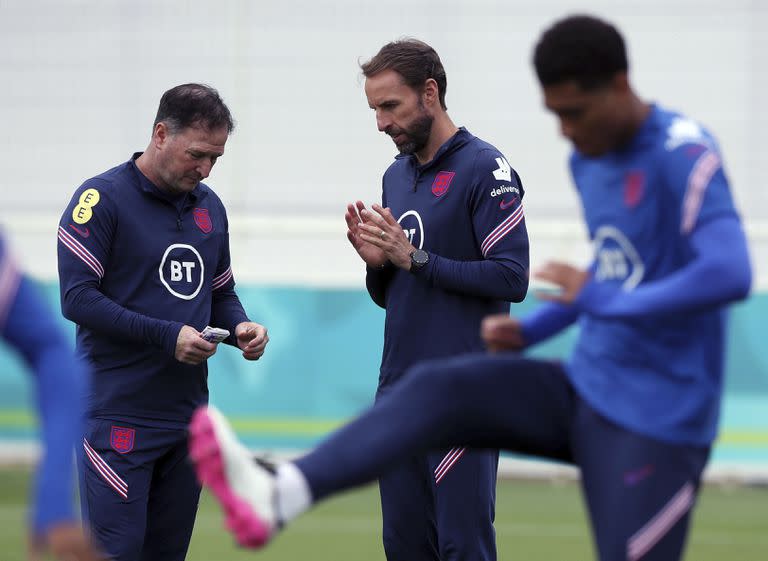 El técnico de Inglaterra, Gareth Southgate (centro) habla con su asistente Steve Holland durante un entrenamiento en Burton upon Trent, el miércoles 30 de junio de 2021 (Nick Potts/PA via AP)