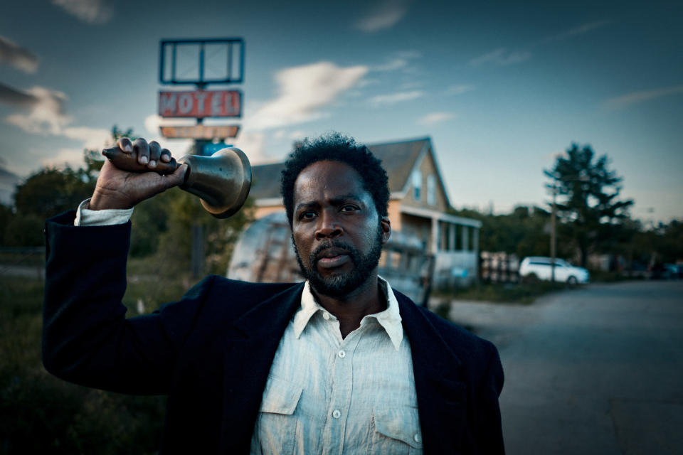 Harold Perrineau shakes a large bell through a town at dusk