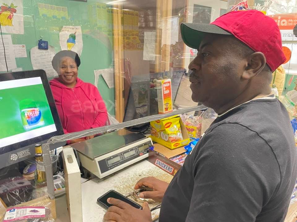 Fifi's Grocery owner Lisia Jean-Baptiste is behind the counter while one of the regular customers, Bartol Artelis, makes a purchase.