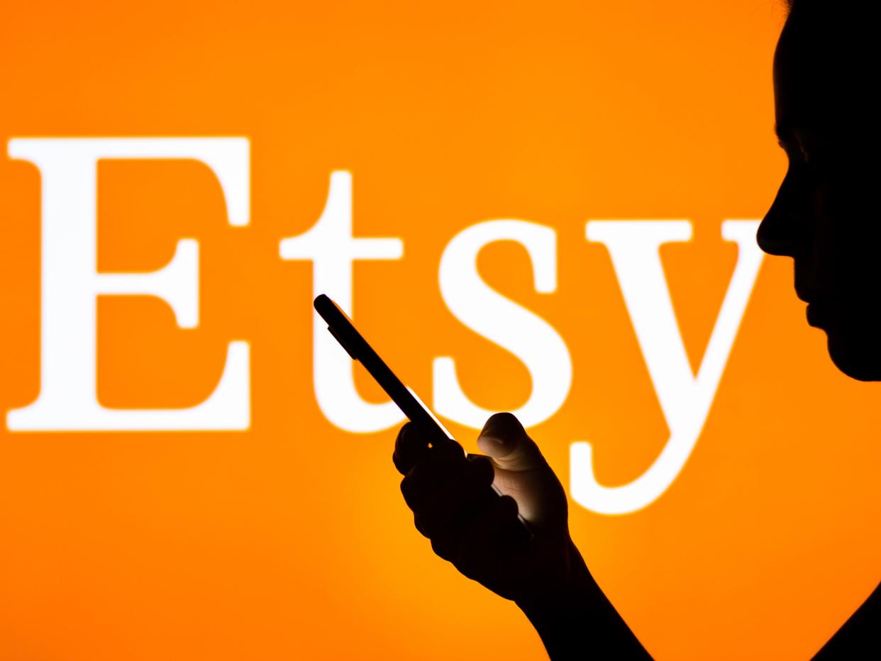 A silhoutte of a person holding a phone in front an orange screen with a white logo that says "Etsy"