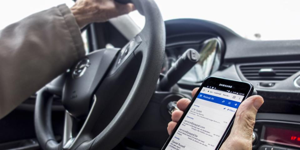 irresponsible man at steering wheel checking messages on smart phone while driving car on road