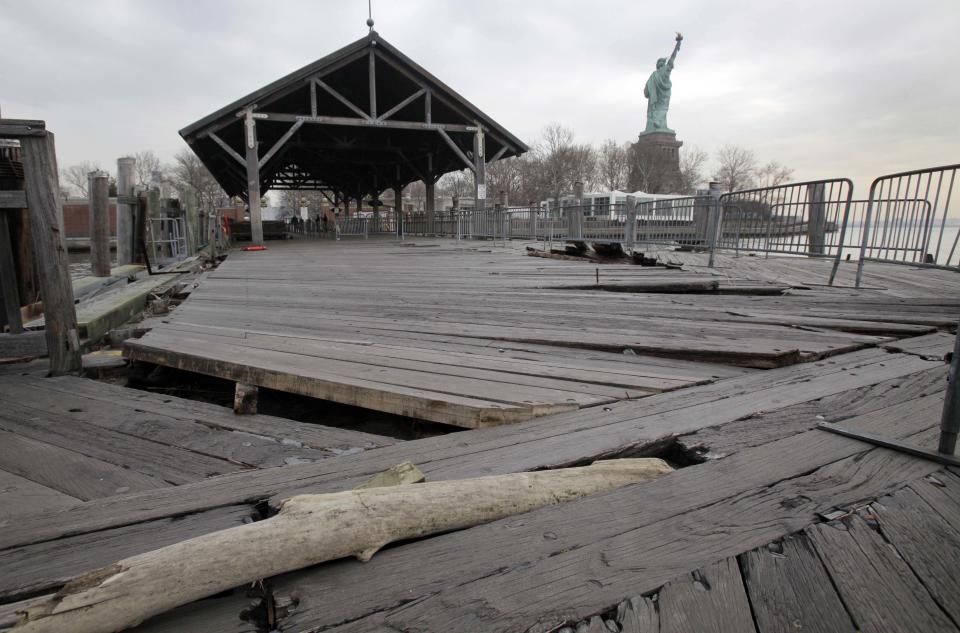 FILE- In this Nov. 30, 2012 file photo, boards of the passenger dock of Liberty Island in New York are askew, damaged from Superstorm Sandy. After hundreds of National Park Service workers from as far away as California and Alaska spent weeks cleaning and making repairs, the island will reopen to the public on Independence Day, July 4, 2013. (AP Photo/Richard Drew, File)