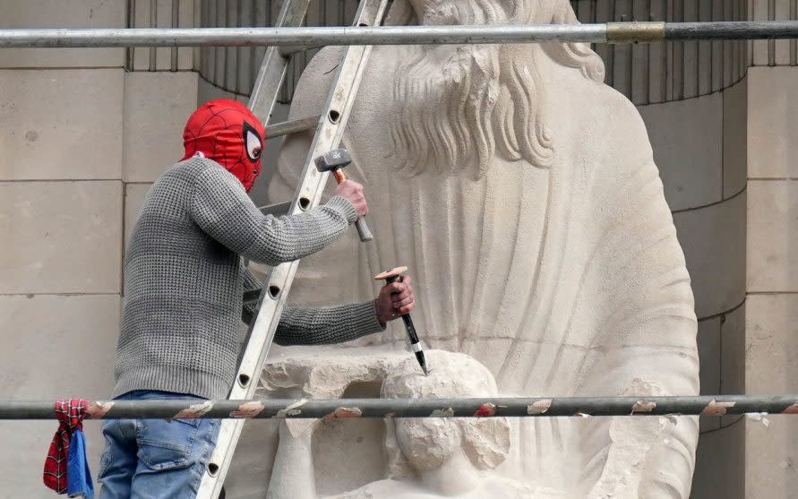 A man wearing a Spider-Man mask uses a hammer and chisel to damage the Prospero and Ariel statue - Jonathan Brady/PA 
