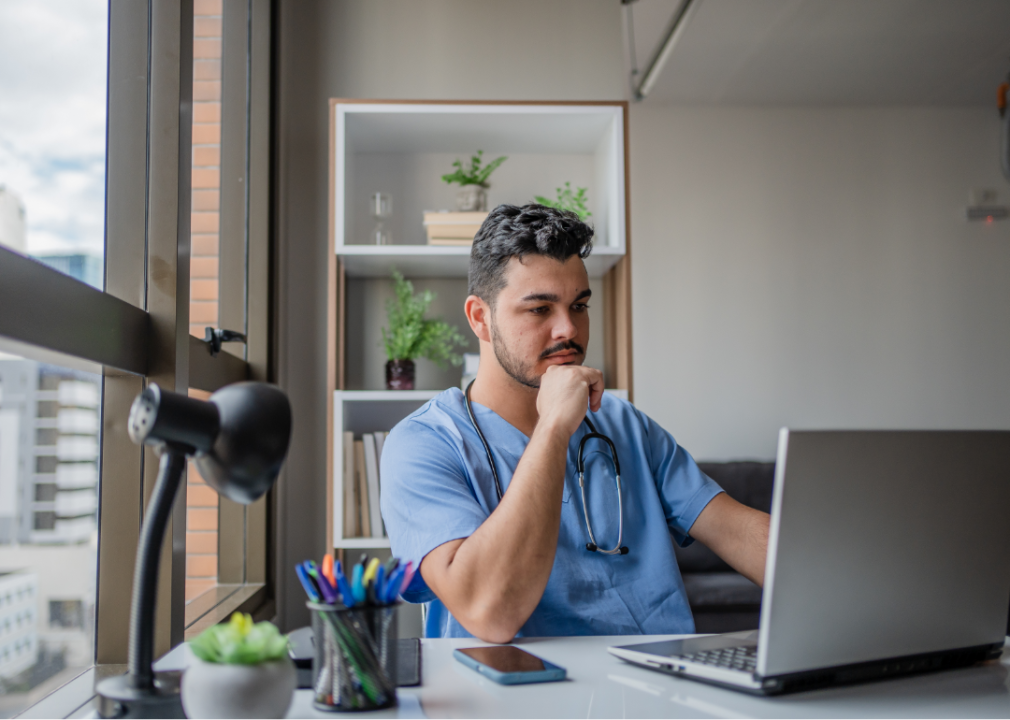 man wearing medical scrubs looking at computer in office