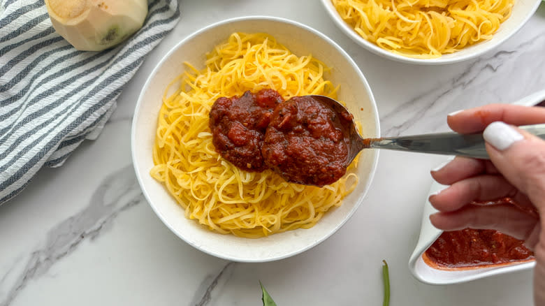 hand adding sauce to noodles