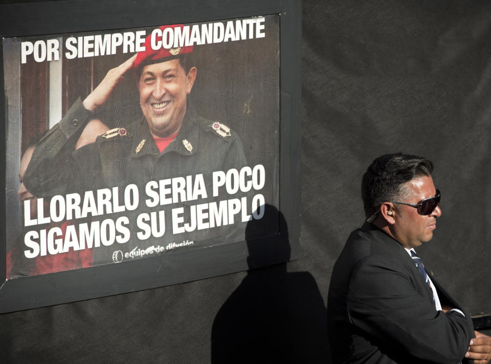 A security officer stands guard near a poster of late Venezuelan President Hugo Chavez that reads in Spanish "forever commander, crying for him is not enough, let's follow his example", at mass at the Villa 21 slum in Buenos Aires, Argentina, Wednesday, March 5, 2014. Argentine President Cristina Fernandez attended the mass in honor of Chavez, one year after the Venezuelan leader's death. (AP Photo/Victor R. Caivano)