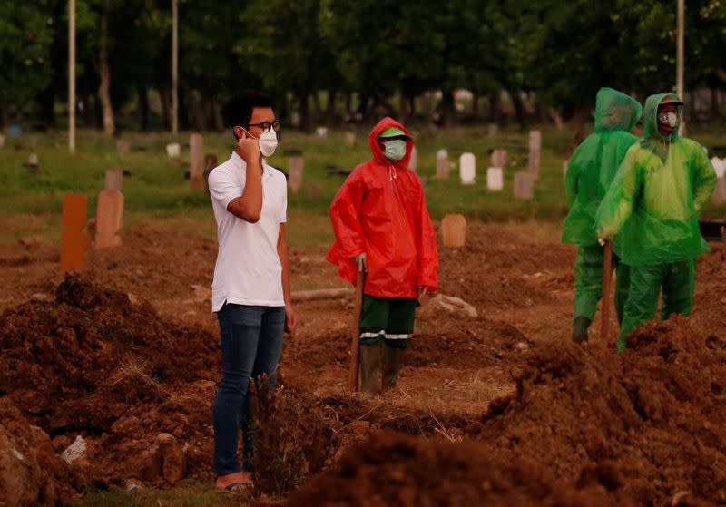 Firos Justin Sumantri, son of Ratih Purwarini, a doctor who passed away due to the coronavirus disease (COVID-19), prays as municipality workers wait, next to his mother's grave during the funeral in Jakarta