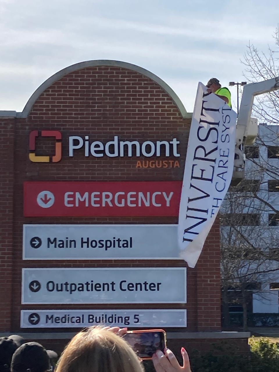 FILE - A worker pulls away the University Health Care System banner to reveal the new Piedmont Augusta name on a sign marking the entrance to the main hospital campus.