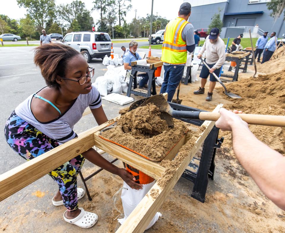 Emmariah Martin holds a bag on Wednesday as a City of Ocala employee fills it with sand. The city established a sandbag stations at Tuscawilla Park.