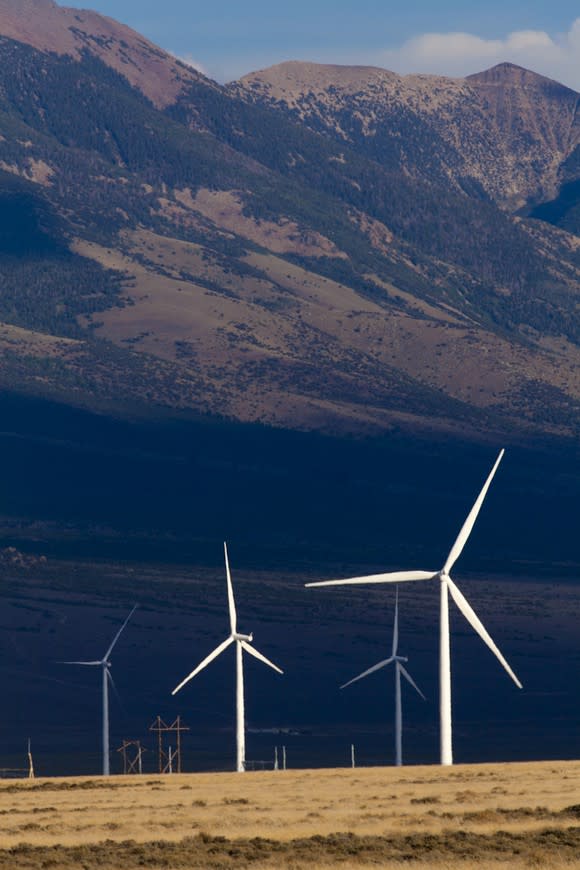 Several wind turbines located in a valley with mountains in the background.