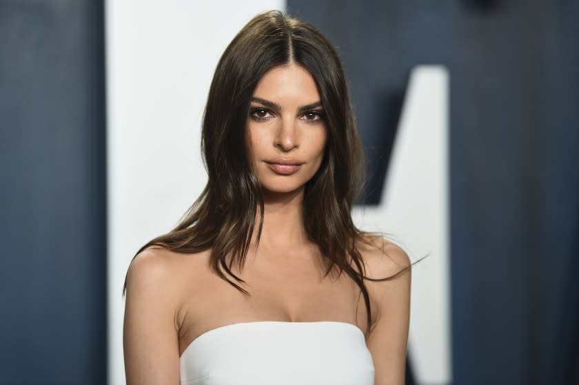 A woman with long brown hair posing in a white dress