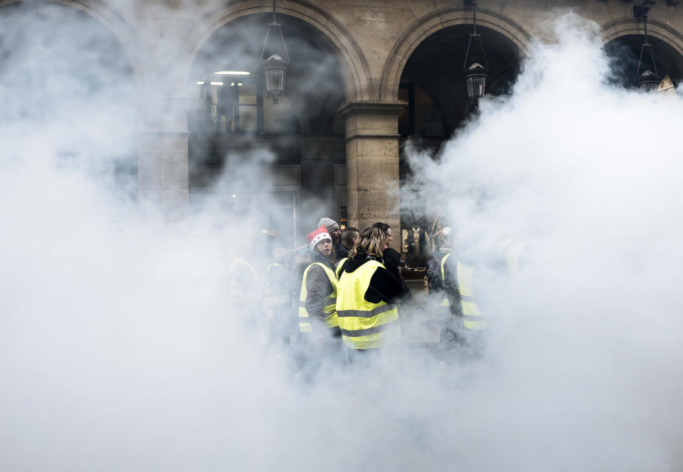 Demonstrators wearing yellow vests walk past by a smoke bomb near the Tuileries gardens in Paris Saturday, Dec. 22, 2018. A few hundred protesters cordoned by police forces did walk across Paris toward the Madeleine Church near the Elysee Palace but were stopped by police in a small adjacent street as some shop owners closed down early. Tempers frayed and police fired tear gas to repel protesters trying to break through the police line. (AP Photo/Kamil Zihnioglu)