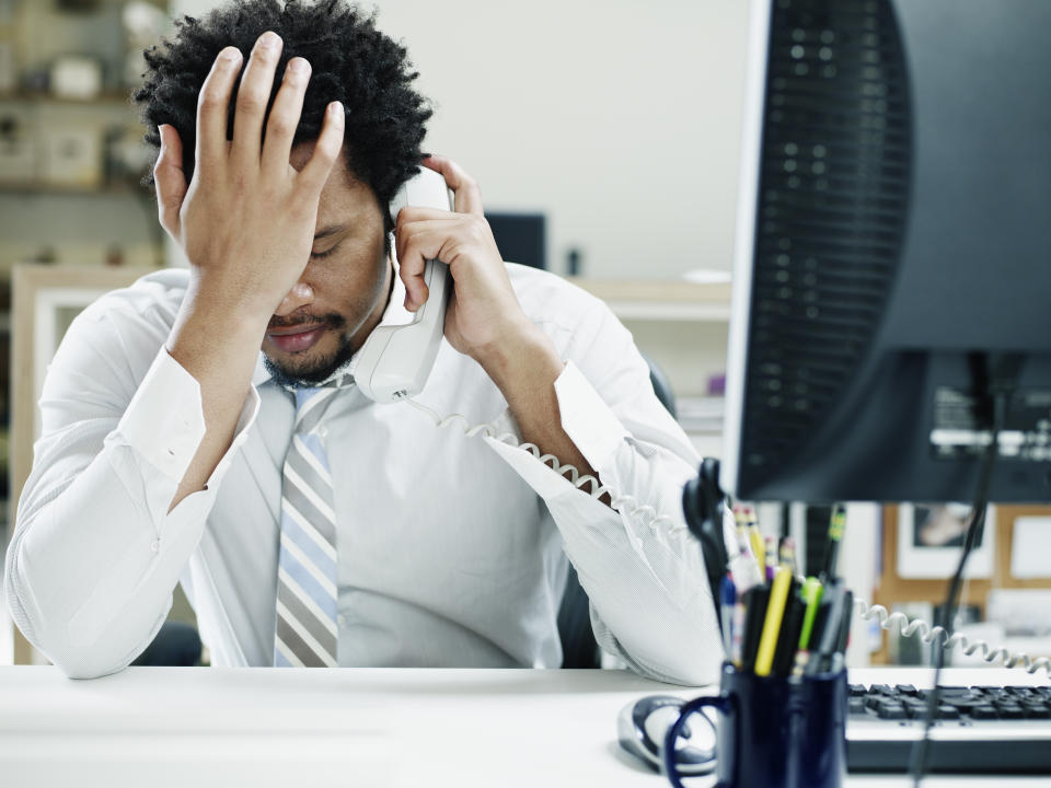 Businessman on phone at desk in office with hand on forehead