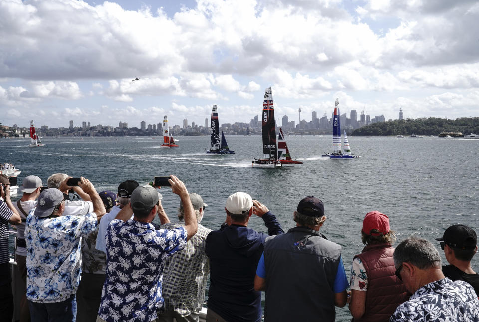 Spectators watch the action from a boat as Britain's boat, center, helmed by Ben Ainslie leads the fleet in the first race of the Sydney SailGP event on Sydney Harbour, Friday, Feb. 28, 2020. (Thomas Lovelock/SailGP via AP)