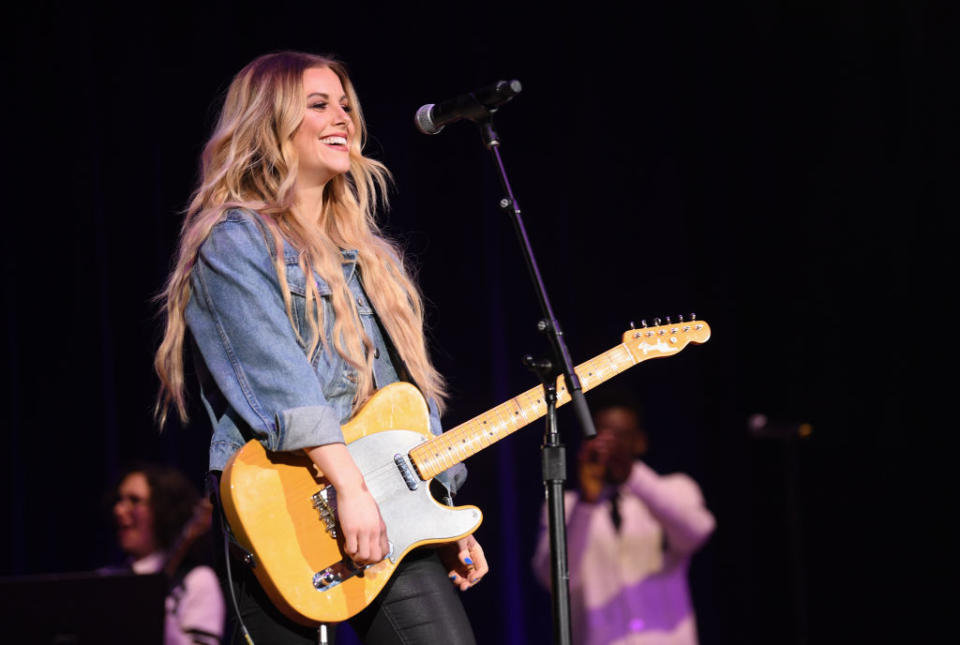 Lindsay with guitar singing on stage, denim jacket, joyous expression