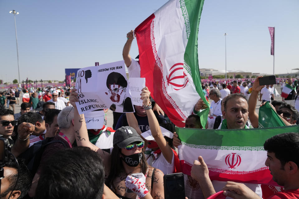 Supporters wave Iranian flags and a woman holds up a sign reading "Freedom for Iran, No to Islamic Republic", ahead of the World Cup group B soccer match between Wales and Iran, at the Ahmad Bin Ali Stadium in Al Rayyan, Qatar, Friday, Nov. 25, 2022. (AP Photo/Jin-Man Lee)