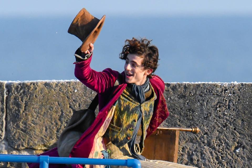 Lyme Regis, Dorset, UK.  12th October 2021.  Scenes for the new Wonka movie starring Timothée Chalamet being filmed on The Cobb harbour at Lyme Regis in Dorset this afternoon.  Timothée Chalamet who is playing the young Willy Wonka, is seen riding on top of a van roof. Picture Credit: Graham Hunt/Alamy Live News