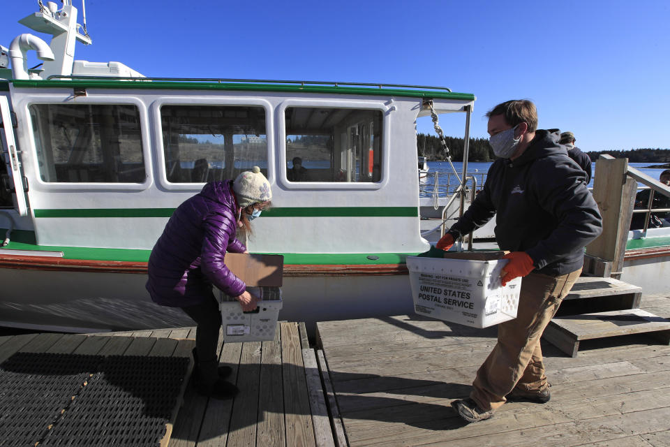 In this Wednesday, May 6, 2020, photo, postmistress Donna DeWitt, left, and mail boat captain Tent Quinby exchange boxes of incoming and outgoing mail on a dock on Isle Au Haut, Maine. Mail service is essential to the 70 or so year-round island residents, who mostly work in the fishing industry. (AP Photo/Robert F. Bukaty)