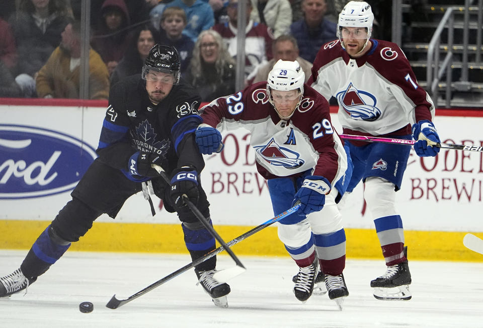 Toronto Maple Leafs center Auston Matthews, left, fights for control of the puck with Colorado Avalanche center Nathan MacKinnon, right, as defenseman Devon Toews looks on in the first period of an NHL hockey game Saturday, Feb. 24, 2024, in Denver. (AP Photo/David Zalubowski)