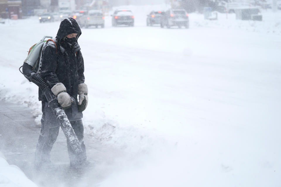 A man blows snow off a sidewalk Wednesday, Dec. 21, 2022, in Minneapolis. (AP Photo/Abbie Parr)