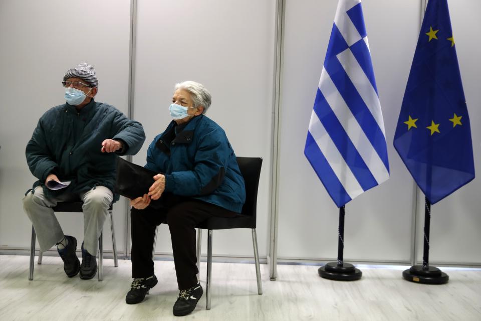 An elderly couple wait at the vaccination mega center in Athens, Monday, Feb. 15, 2021. The Promitheas center, which has started operating Monday, will host 96 vaccination points and when fully developed, an estimated of 150,000 vaccinations per month could be conducted. (AP Photo/Thanassis Stavrakis)