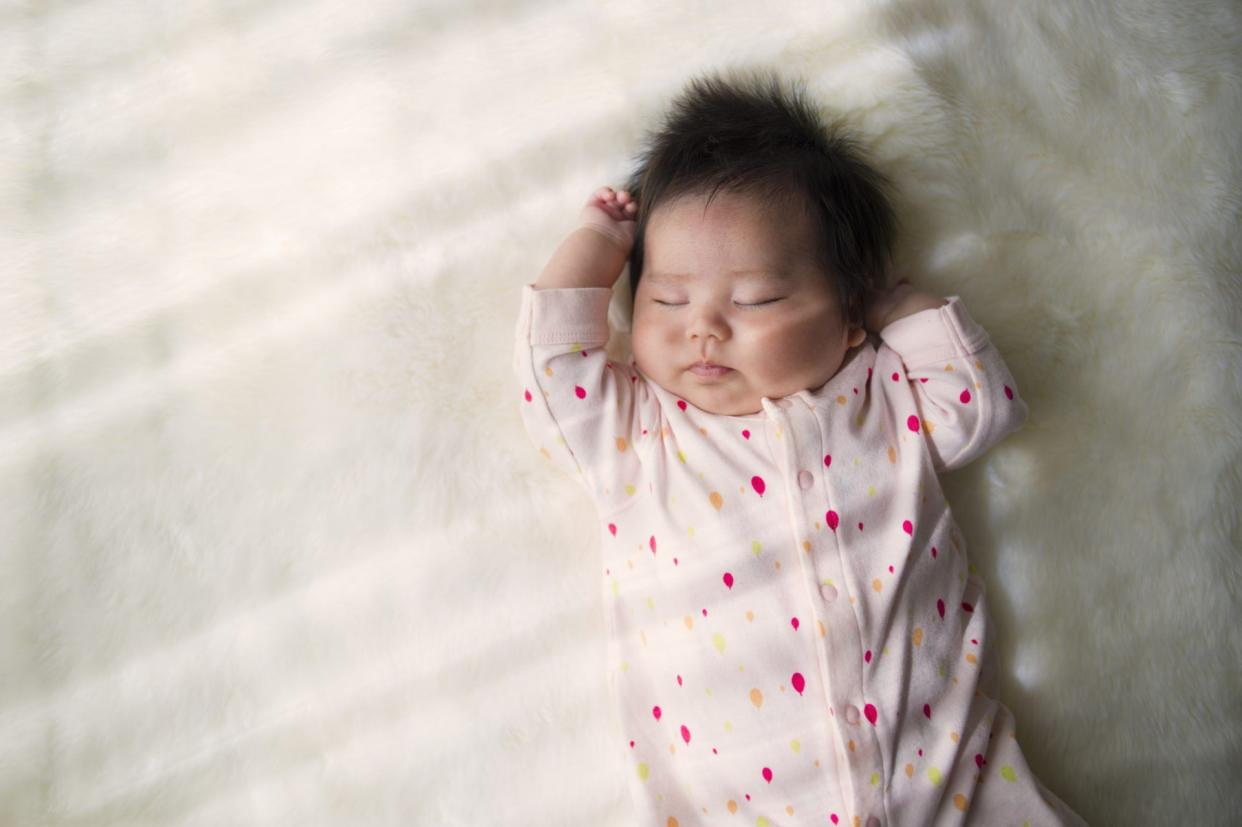 Newborn baby sleeping on a white rug.