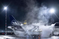 A Lufthansa aircraft is de-iced at Frankfurt Airport, Germany, early Wednesday, Jan. 17, 2024. Heavy snowfalls and freezing rain across Germany Wednesday led to the cancellation of hundreds of flights and trains, crashes on icy roads, and school closures. (Boris Roessler/dpa via AP)