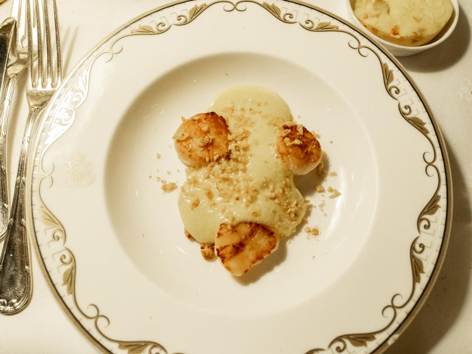 A scallop appetizer on a white plate with gold trimmings