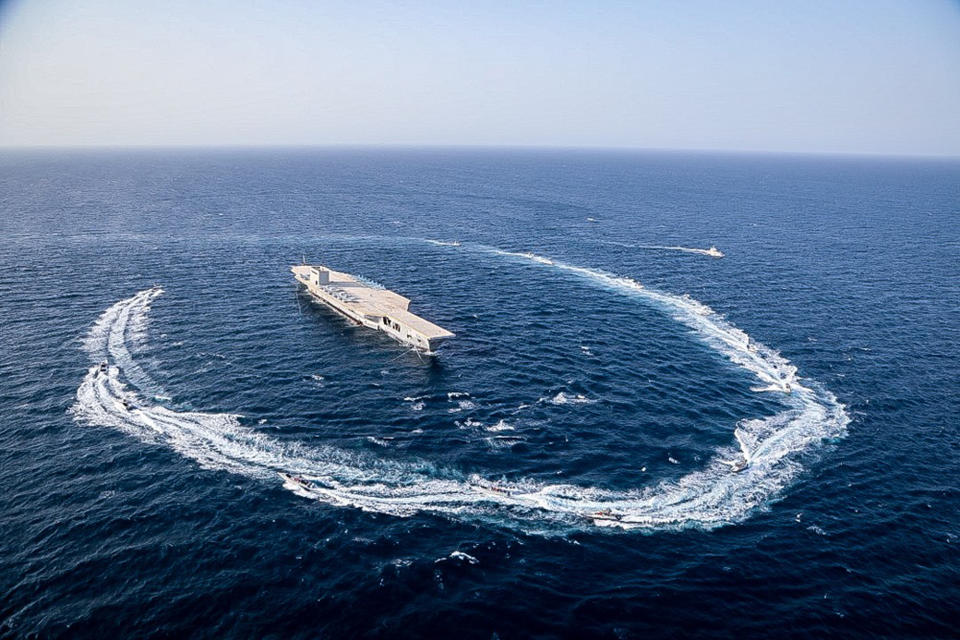 In this photo released Tuesday, July 28, 2020, by Sepahnews, Revolutionary Guard's speed boats circle around a replica aircraft carrier during a military exercise. Iran’s paramilitary Revolutionary Guard fired a missile from a helicopter targeting the mock-up aircraft carrier in the strategic Strait of Hormuz according to footage aired on state television on Tuesday. Iranian commandos also fast-roped down from a helicopter onto the replica in the footage from the exercise called “Great Prophet 14.” The drill appears aimed at threatening the U.S. amid tensions between Tehran and Washington. (Sepahnews via AP)