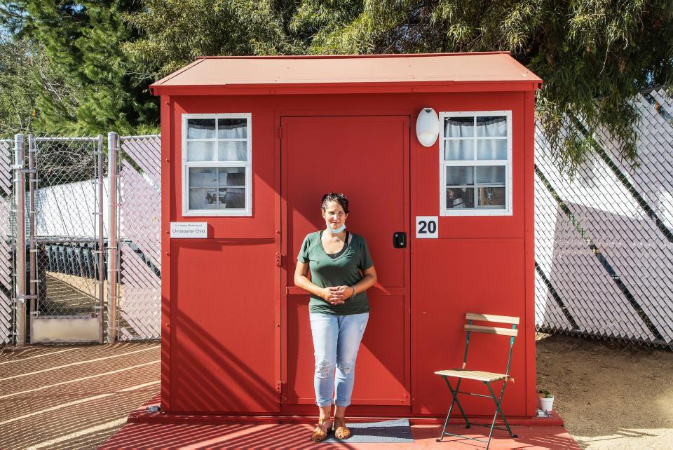 A woman stands outside a small, red home.