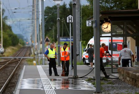 A Swiss police officer stands near workers cleaning a platform after a 27-year-old Swiss man's attack on a Swiss train at the railway station in the town of Salez, Switzerland August 13, 2016. REUTERS/Arnd Wiegmann