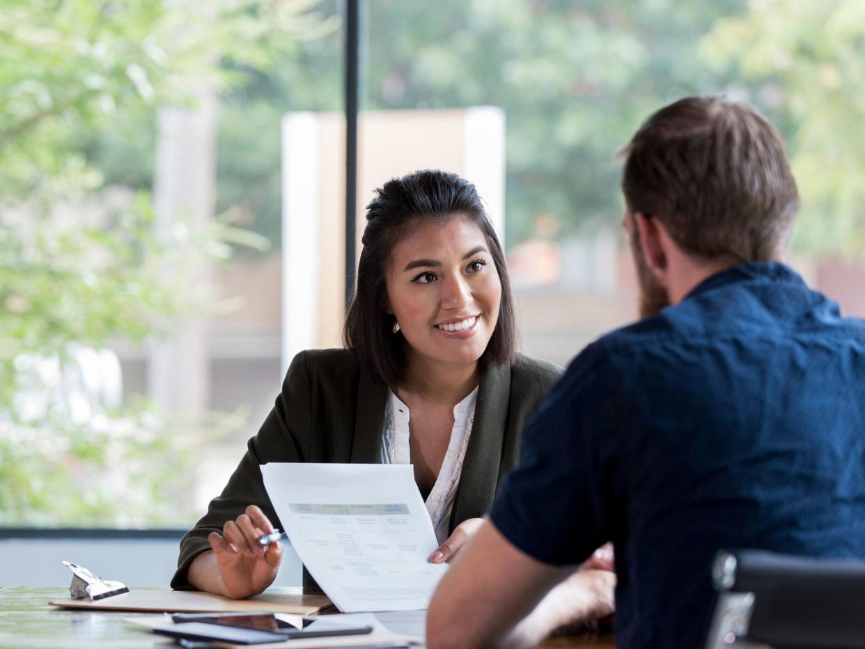 Hispanic businesswoman smiles while showing a document to a male associate.