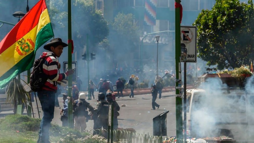 Homre con bandera de Bolivia y con gases lacrimógenos cerca