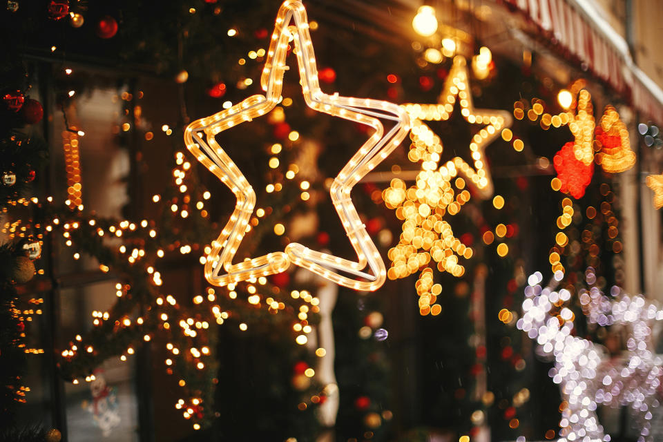 Stylish christmas golden star illumination and fir branches with red and gold baubles, golden lights bokeh on front of building at holiday market in city street. Christmas street decor