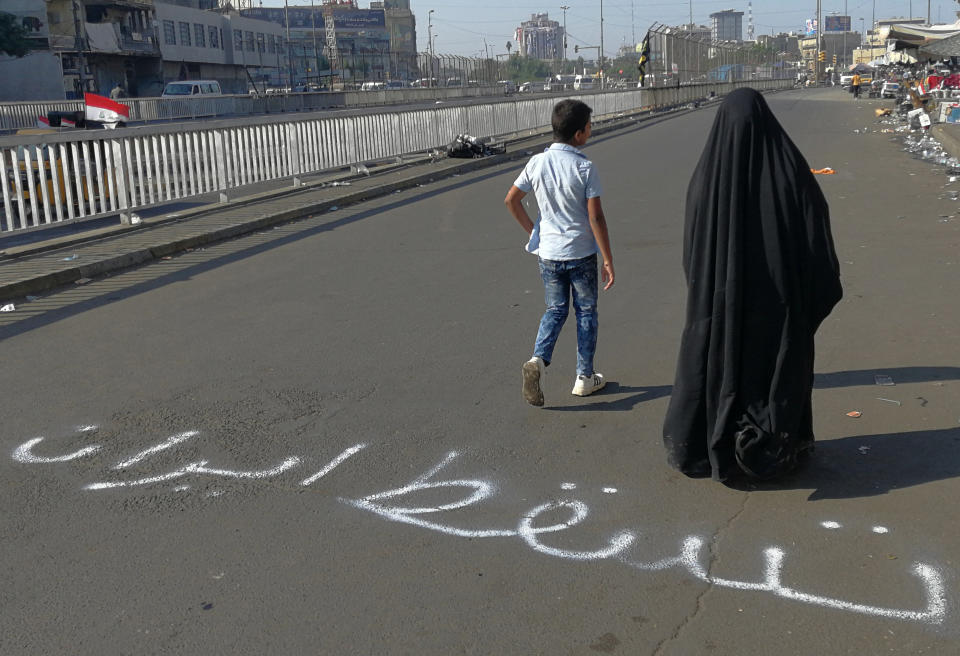 FILE - In this Nov. 1, 2019, file photo, people walk by an Arabic sentence writing on the asphalt reads "Down with Iran" near the site of the protests at Tahrir Square during anti-government ongoing protests in Baghdad, Iraq. Iraqi protesters are mocking Iran’s leaders, firebombing the offices of its local political allies and threatening its diplomatic missions. (AP Photo/Khalid Mohammed, File)