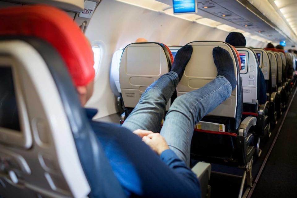 Man relaxing and sleeping during flight with his feet up on the back of the seat, no shoes on