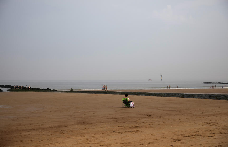 A woman reads a book on a nearly empty beach at the Belgian seaside resort of Knokke, Belgium, Tuesday, Aug. 11, 2020. At the seaside resort of Knokke-Heist, where golf carts with license plates ply well-kept streets, there was ample room to stretch out on the local beach this week. Local authorities have banished day trippers from Belgian cities or France from its 15-kilometer (10-mile) stretch of sands until the heat wave is over. (AP Photo/Virginia Mayo)
