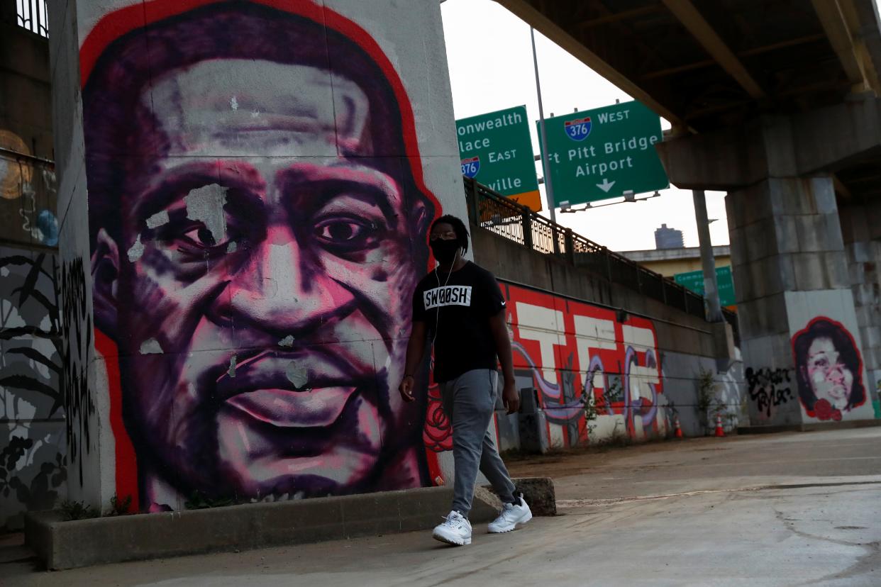 <p>A man wearing a protective face mask walks by murals of George Floyd and Breonna Taylor in Pittsburgh</p> (REUTERS)