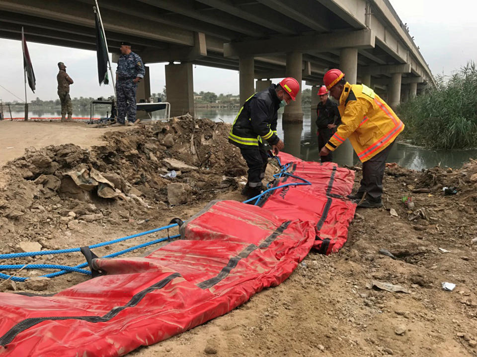 In this Saturday, Nov. 3, 2018 photo, officials prepare to lay a cordon in the water to gather dead fish near the town of Hindiyah, 80 kilometers (50 miles) south of Baghdad, Iraq. Officials and fishermen are at a loss to explain how hundreds of tons of carp have suddenly died in fish farms in the Euphrates River, fueling anxieties about soaring water pollution. Local authorities used excavators to skim dead fish from the river surface, where residents and local farmers have long complained about substandard water management. (AP Photo/Ali Abdul Hassan)