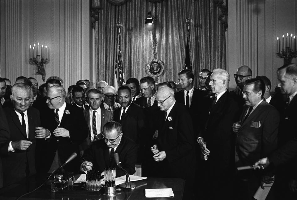 President Lyndon Johnson, surrounded by officials, and with the Rev.Martin Luther King Jr. behind him, signs the Civil Rights Act. 