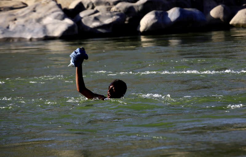 FILE PHOTO: An Ethiopian fleeing the ongoing fighting in Tigray region, lifts his clothes as he crosses the Setit river on the Sudan-Ethiopia border in Hamdayet village in eastern Kassala state