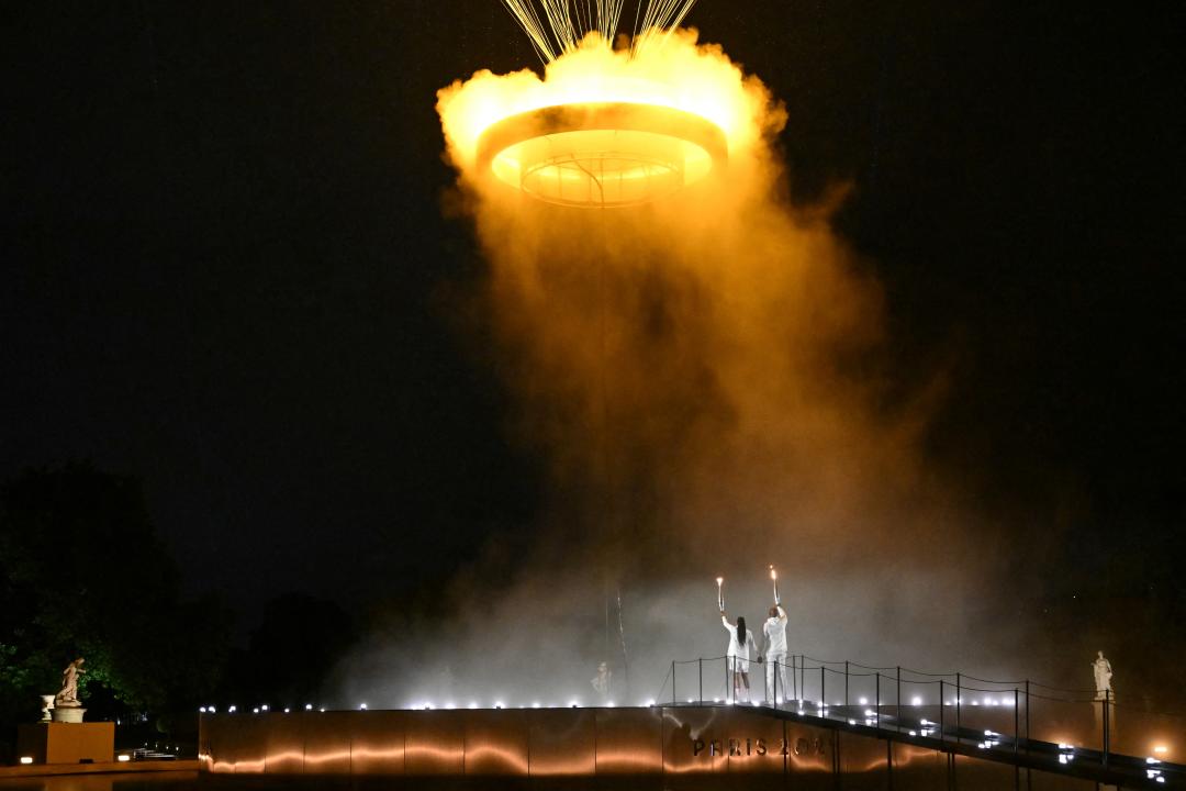 TOPSHOT - The cauldron, with the Olympic flame lit, lifts off while attached to a balloon as the torchbearers French former sprinter Marie-Jose Perec and French judoka Teddy Riner stand in front during the opening ceremony of the Paris 2024 Olympic Games at the Jardin des Tuileries (Tuileries Garden) in Paris on July 26, 2024. (Photo by MOHD RASFAN / AFP) (Photo by MOHD RASFAN/AFP via Getty Images)