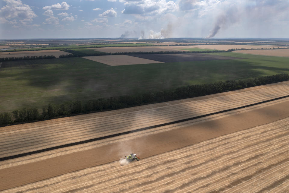 Smoke rises in the background during a fierce battle on the frontline, as a farmer collects harvest in a field in the Dnipropetrovsk region, Ukraine, Monday, July 4, 2022. An estimated 22 million tons of grain are blocked in Ukraine, and pressure is growing as the new harvest begins. The country usually delivers about 30% of its grain to Europe, 30% to North Africa and 40% to Asia. But with the ongoing Russian naval blockade of Ukrainian Black Sea ports, millions of tons of last year’s harvest still can’t reach their destinations. (AP Photo/Efrem Lukatsky)