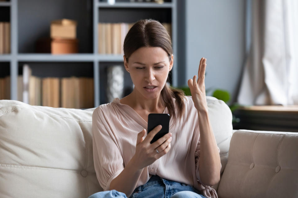 A woman looking at her phone with her hand up in frustration