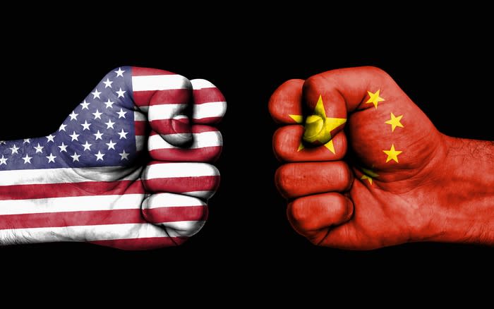 Two fists squaring off, with one decorated as the American flag, and the other as the Chinese flag.