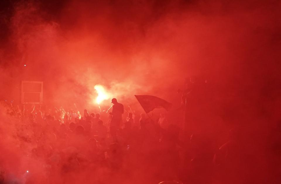 Liverpool supporters are encompassed in smoke as they celebrate outside of Anfield Stadium in Liverpool, England, on Thursday, June 25, 2020, after their team clinched the English Premier League title. Liverpool took the title after Manchester City failed to beat Chelsea on Wednesday evening. (AP photo/Jon Super)